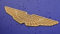 Aston Martin logo in gold against a closeup of a purple car