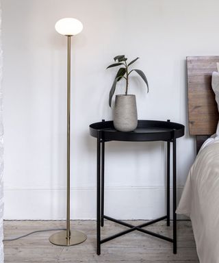 Slim brass floor lamp with orb shape head besides round, black tray table with potted plant.