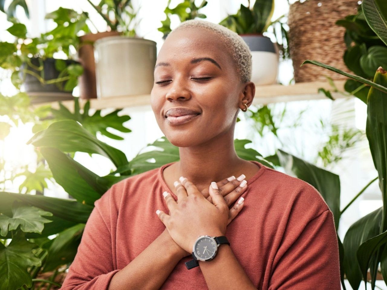 A peaceful looking woman smiles in a room full of plants