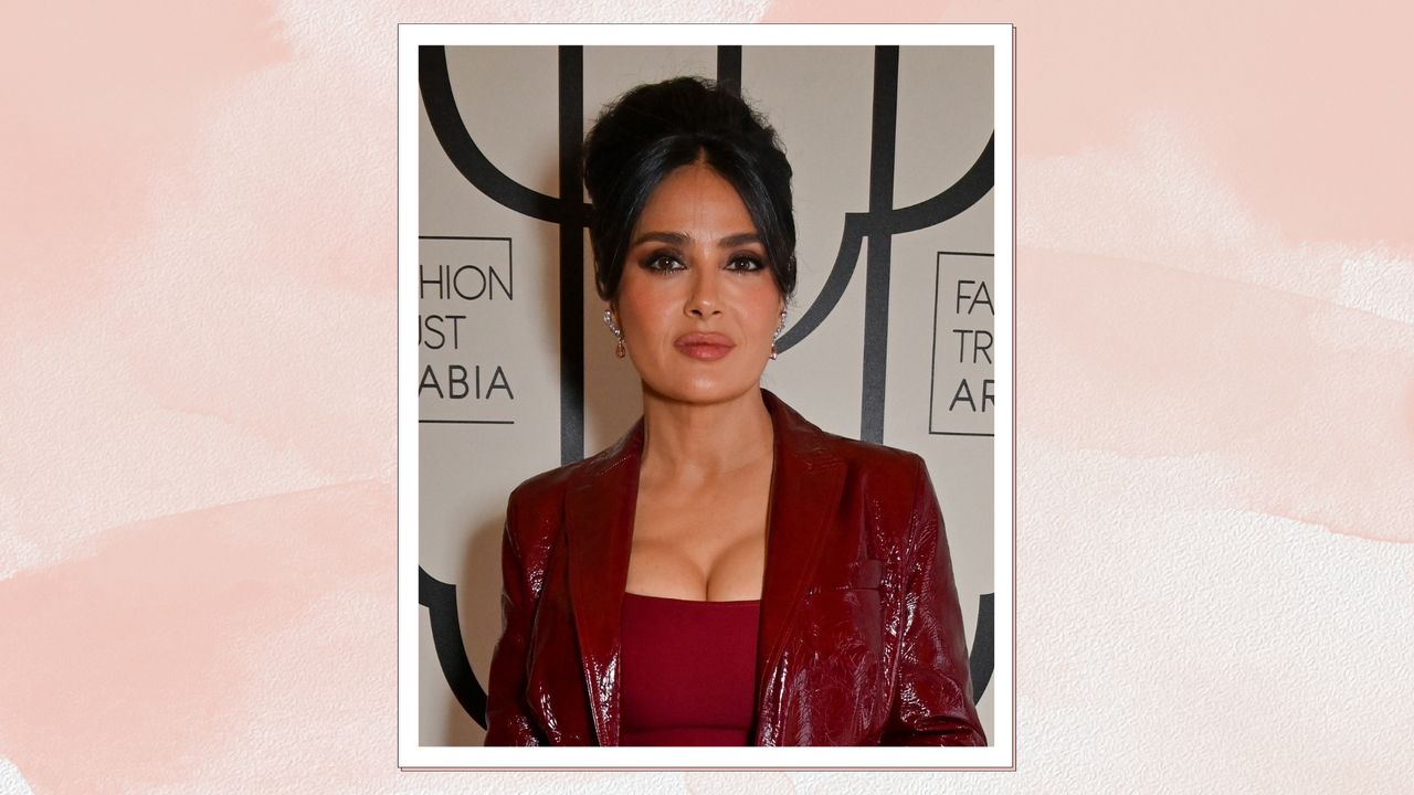 Portrait of Salma wearing a burgundy dress and leather blazer, with a bouffant updo and a neutral lipstick