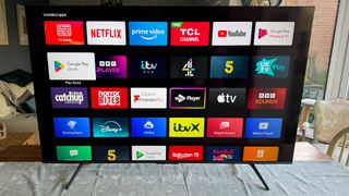 TCL C655K (55C655K) 55-inch TV on wooden table and white runner showing Android TV OS on screen