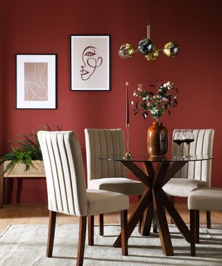 A burgundy dining room with three white plush chairs, a circular table with flowers on, and two pink wall art prints