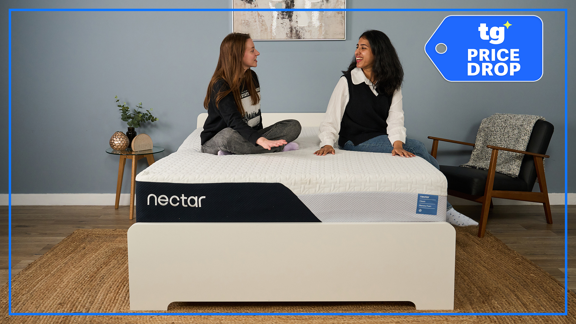 Nectar Classic Memory Foam Mattress on a wooden bd frame, with two Tom's Guide mattress testers sitting on top of it. A blue Tom's Guide Price Drop badge is overlaid in the top right hand corner