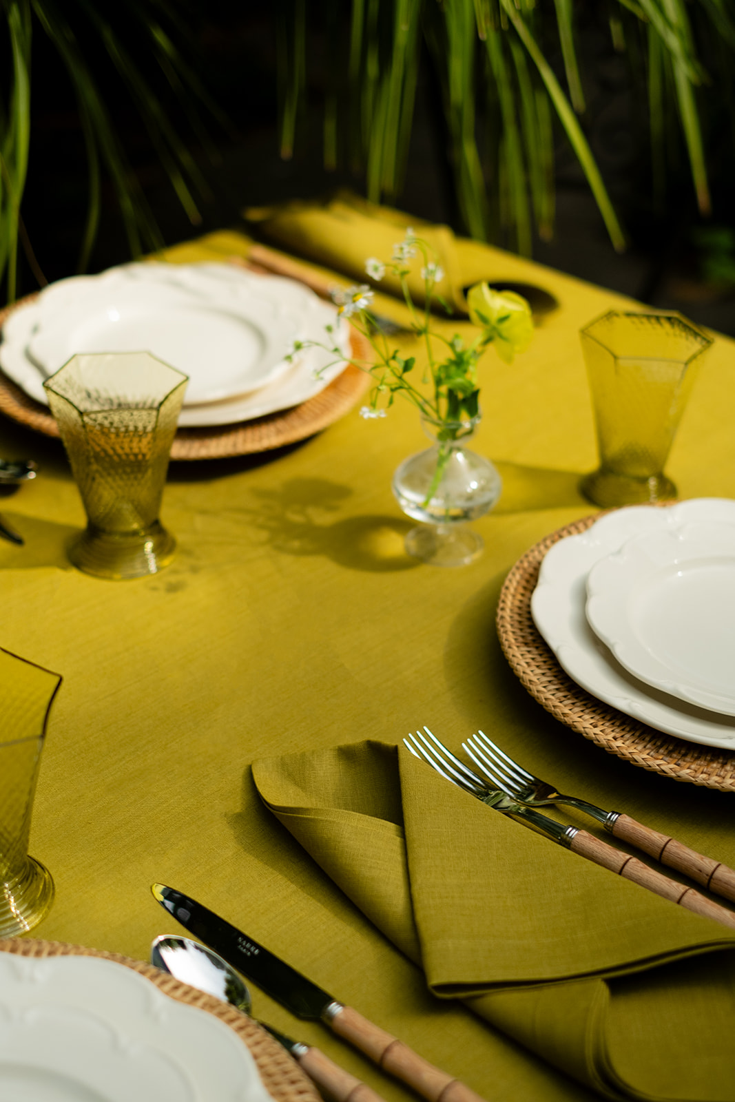 An olive green, color drenched dining table display with matching drinking glasses and white scalloped edge dinner plates, on wicker place mats.