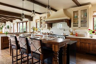 kitchen with pale stone floors and worktops patterned tiled backsplash and dark wood island