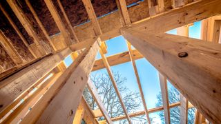 Wooden frame of a residential house construction photographed from the ground floor looking up through the roof trusses at a blue sky 