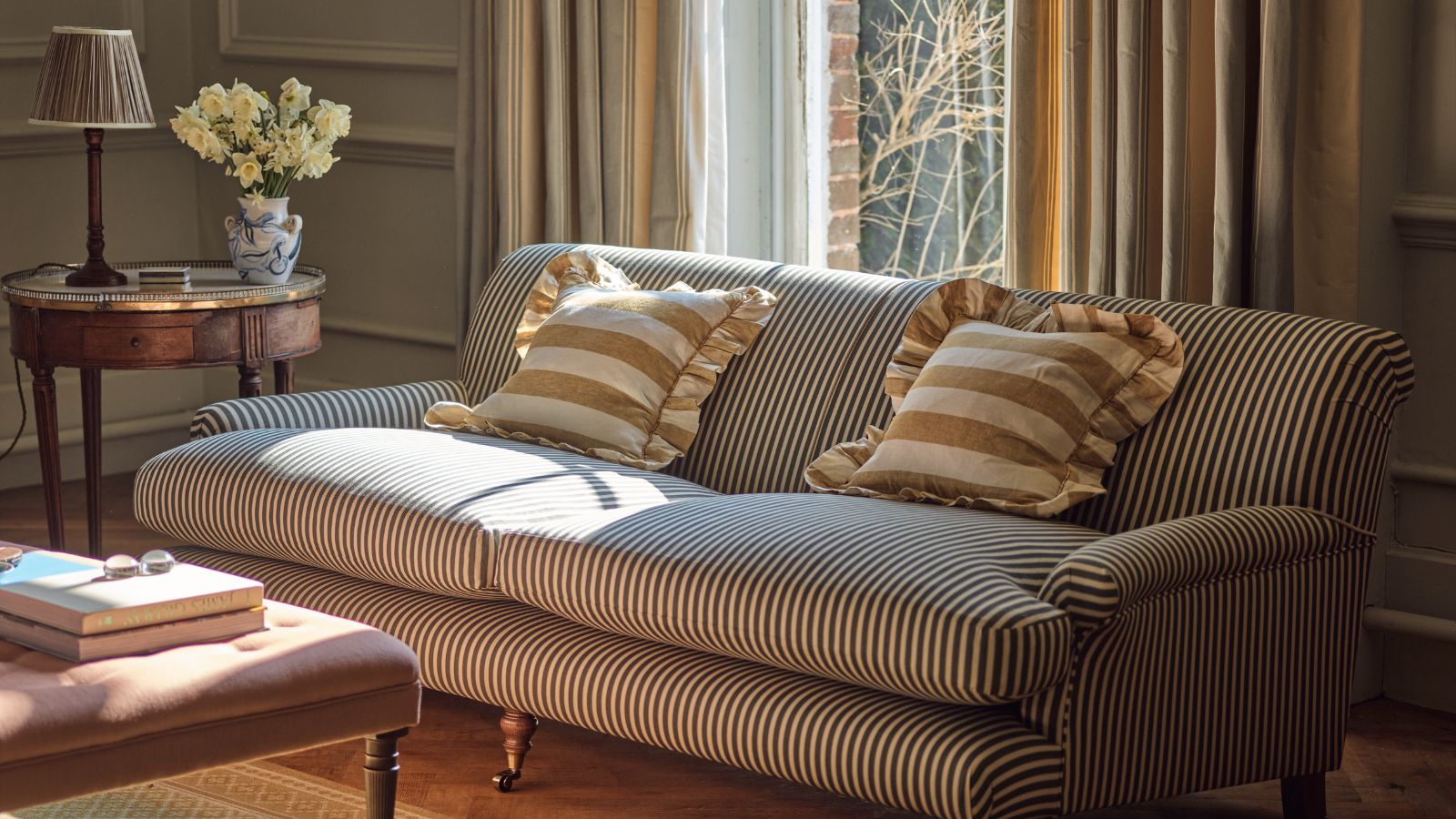 A black and white pinstripe sofa in a traditional living room. A small wooden side table with a lamp and vase of flowers beside it. White and yellow striped cushions on it. 