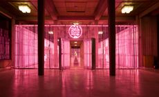 Entrance to the 24 hour Prada museum featuring a steel cage backlit by vertical rows of pink neon tubes