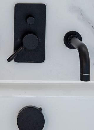 Close up image of black bathroom tap and wall mounted dials