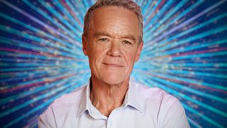 Stefan Dennis smiling for the camera with a glittery blue background behind him
