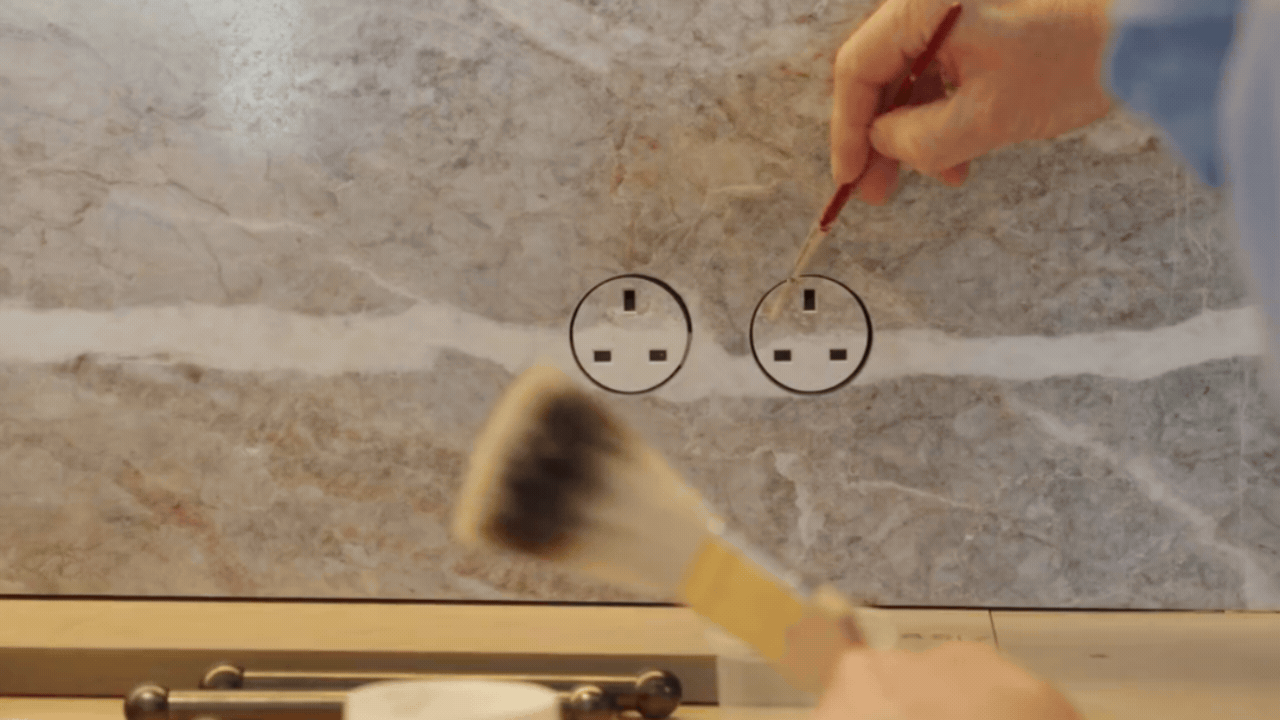 a man painting the plug sockets on a marble backsplash to blend in with the wall 