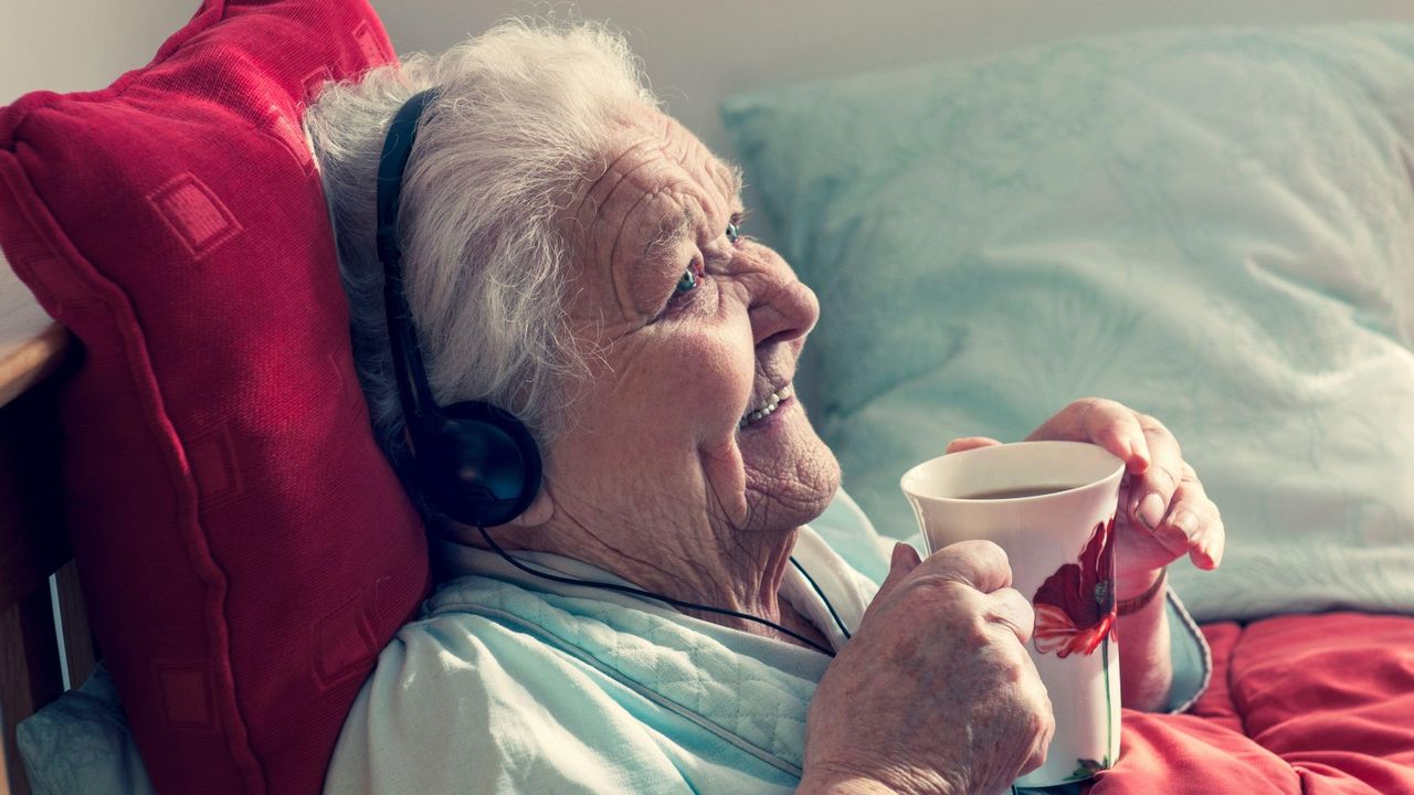 Elderly woman sat listening to music through headphones in care home