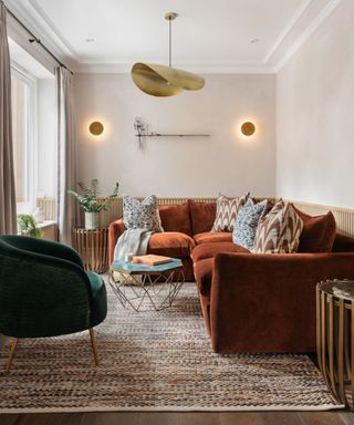 Small sitting room with a large metallic pendant light fitting, terracotta velvet corner sofa and circular wall lights