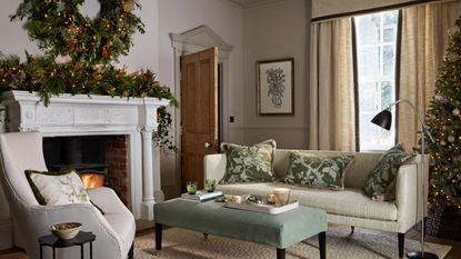  A living room decorated for Christmas with a large wreath made of evergreen foliage and gold baubles, and a garland on the mantlepiece of a traditional fireplace.