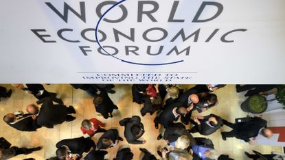 Participants at the World Economic Forum (WEF) annual meeting chat under a sign on January 25, 2012 at the Congress Center in Davos. The world's political and business elite will shelter from