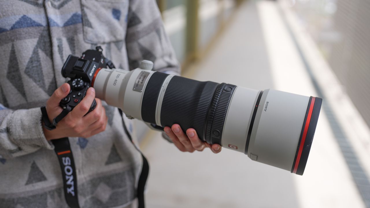 A picture of a man holding the Sony A7R VI camera with the Sony 100-400mm f/4.5 GM lens mounted.