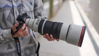 A picture of a man holding the Sony A7R VI camera with the Sony 100-400mm f/4.5 GM lens mounted.