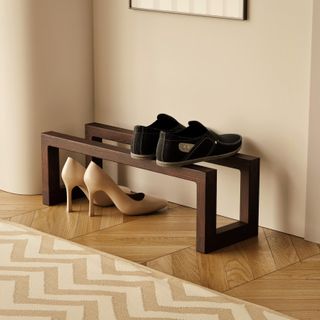 A minimalist show organizing rack with two wooden bars. A pair of sneakers on top and a pair of heels below. 