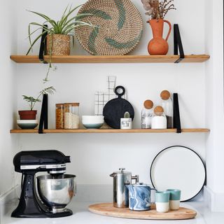 White kitchen worktop and oak shelving furnished with storage containers, trinkets and black KitchenAid stand mixer