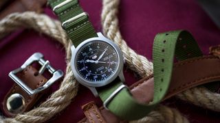 Still-life watch photograph of watch with green strap on a maroon canvas bag surrounded by rope and leather straps