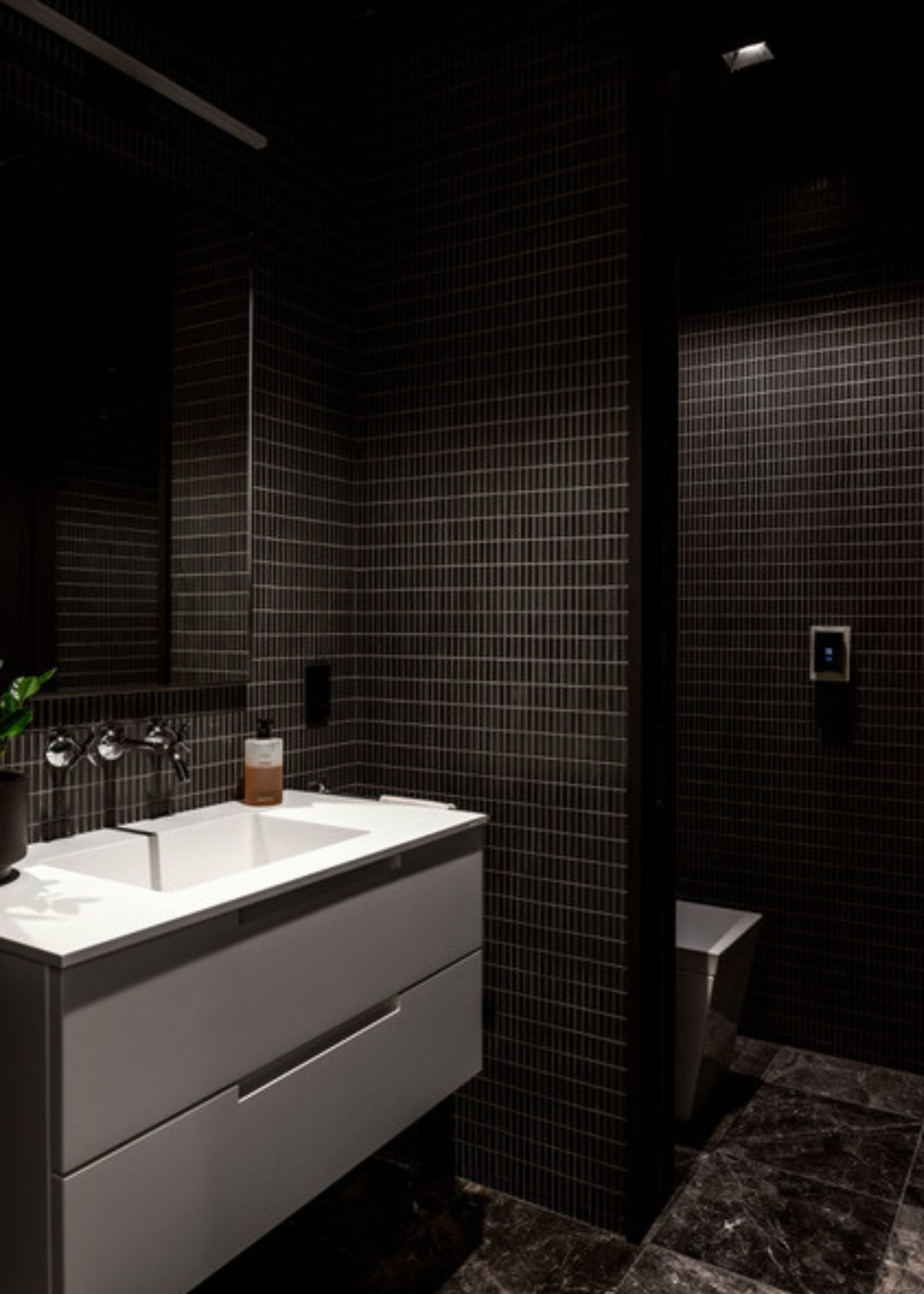 A black bathroom with black tiles on the walls and floor and a bright white sink to add contrast to the space