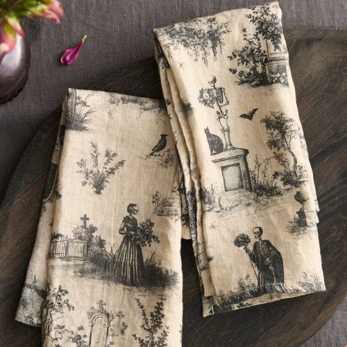 Cream linen napkins in a toile print depicting skeletons, black cats, gravestones and bats