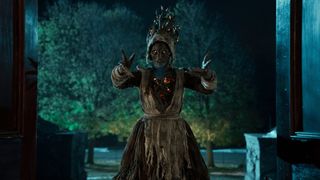 A witch stands in a doorway with arms outstretched in Dreams in the Witch House on Netflix