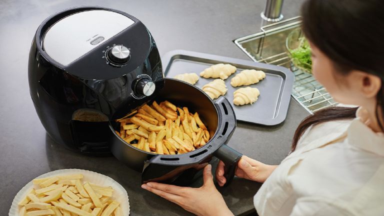 Woman using airfryer to cook chips, with other ingredients on workbench