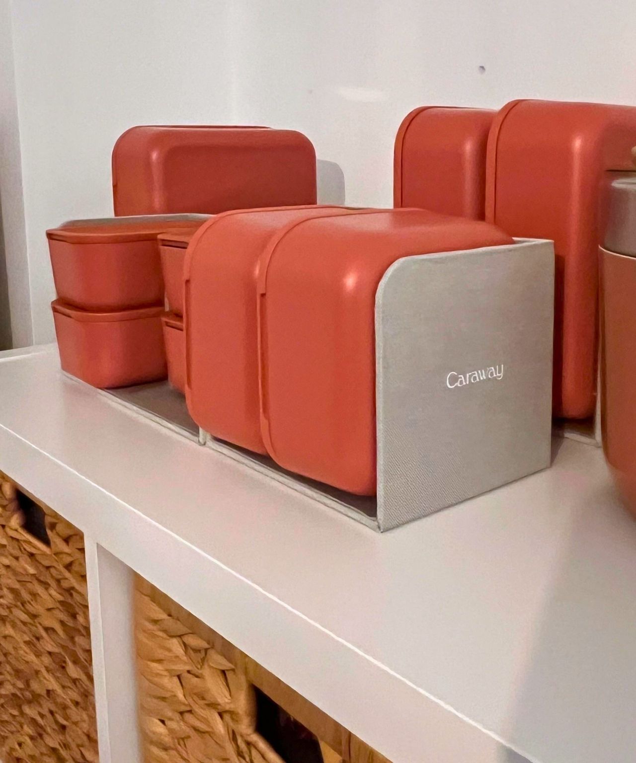 The whole Caraway non toxic food container set in terracotta, shown here stacked neatly in its included organizers, on top of a KALLAX IKEA unit