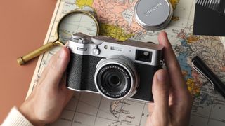 Fujifilm X100VI camera held between two hands over a map