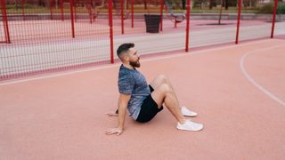 Man in a park sitting down with knees bent and hands placed behind his hips