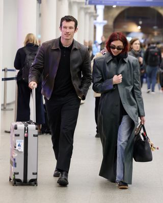 Dua Lipa and Callum Turner walking through a train station in matching travel outfits