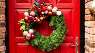 Red wooden front door decorated with modern bauble and spruce Christmas wreath