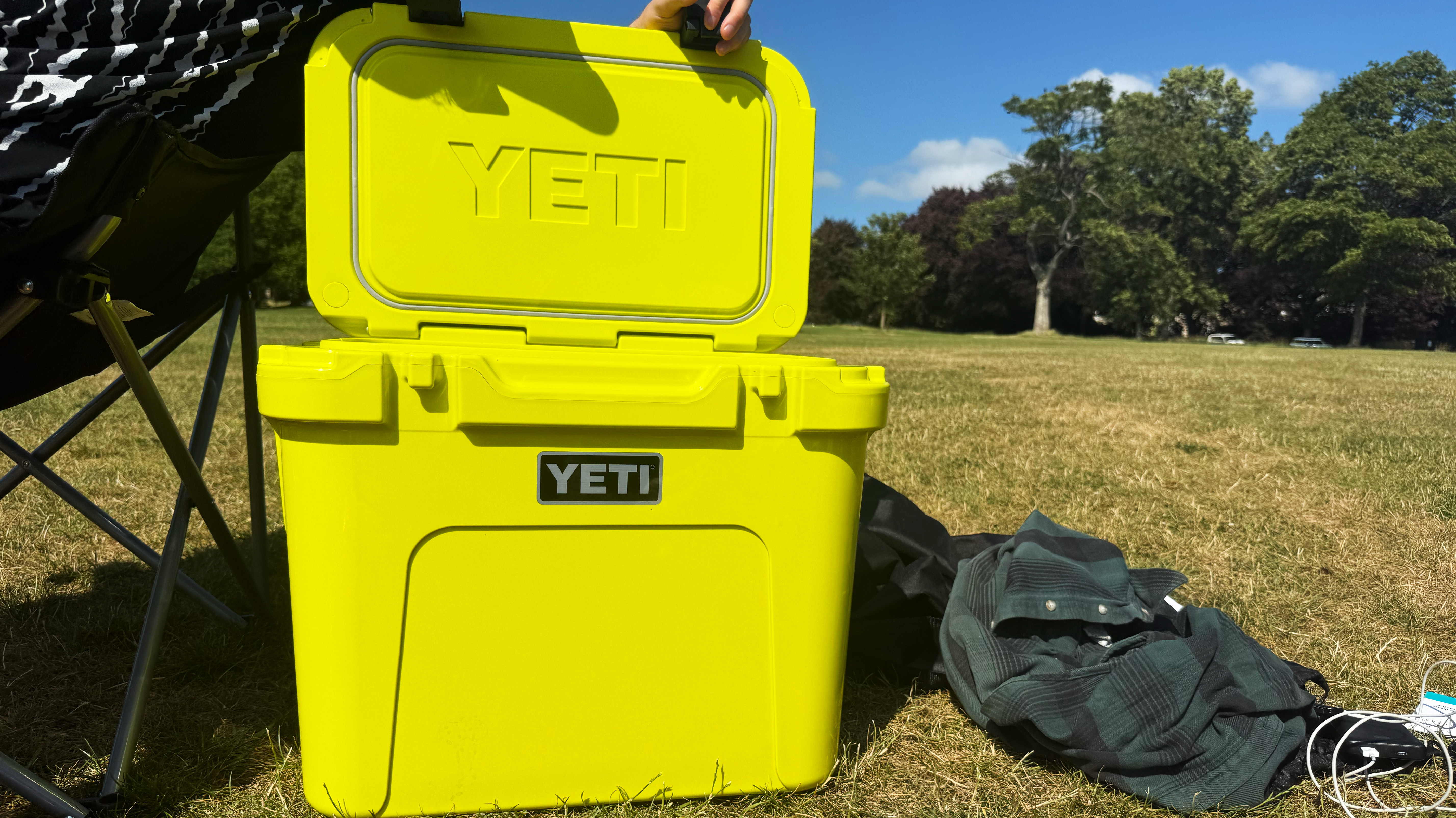 the Yeti Roadie cooler in yellow in a park, resting on top of grass with trees in the background and blue sky