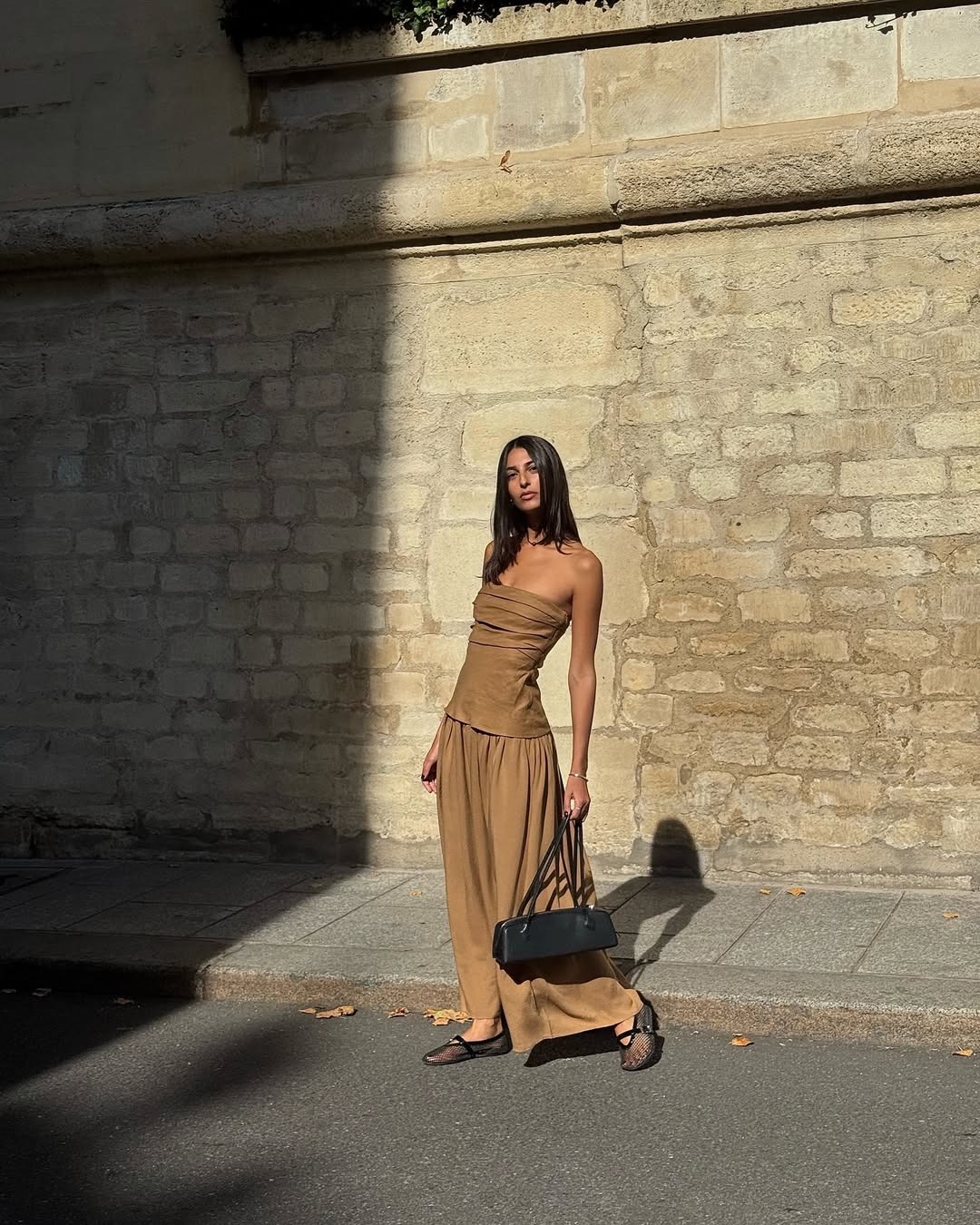 Woman wears beige drape top and trousers, Alaia bag and mesh ballet flats.