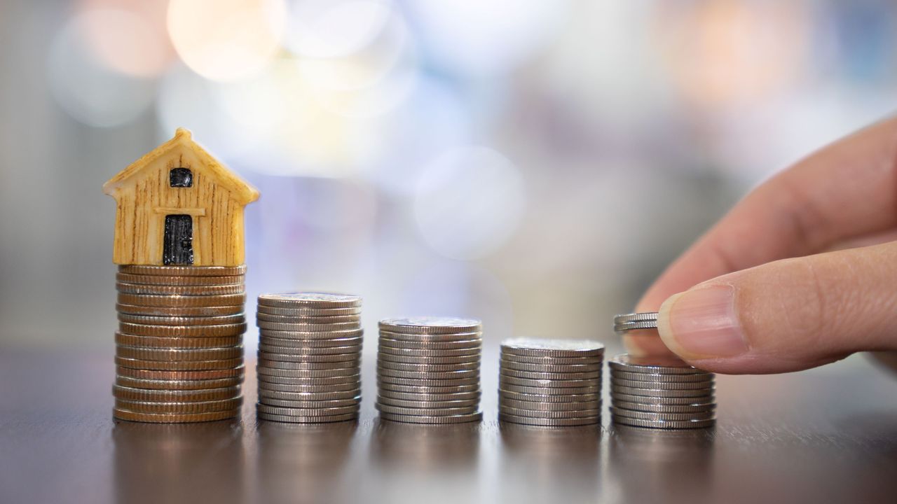 A stack of coins with a small wooden house figure representing a down payment. 