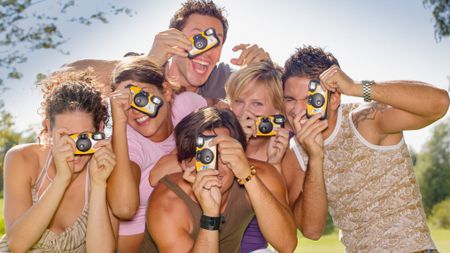 Group of young people aiming their disposable cameras towards the viewer