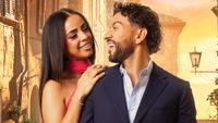 Jessy Peralta and Vittorio Palchetti smiling at each other in an official cast picture. He's wearing a black suit and she's wearing a red dress. He has a diamond-studded earring.