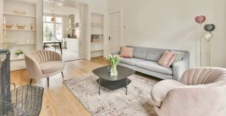 neutral living room with pale gray sofa and pastel pink scalloped armchairs to match to show how to make a living room look expensive by choosing a single look throughout