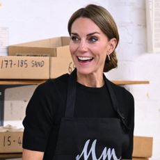 Kate Middleton wearing a black shirt and apron with her hair in a knot