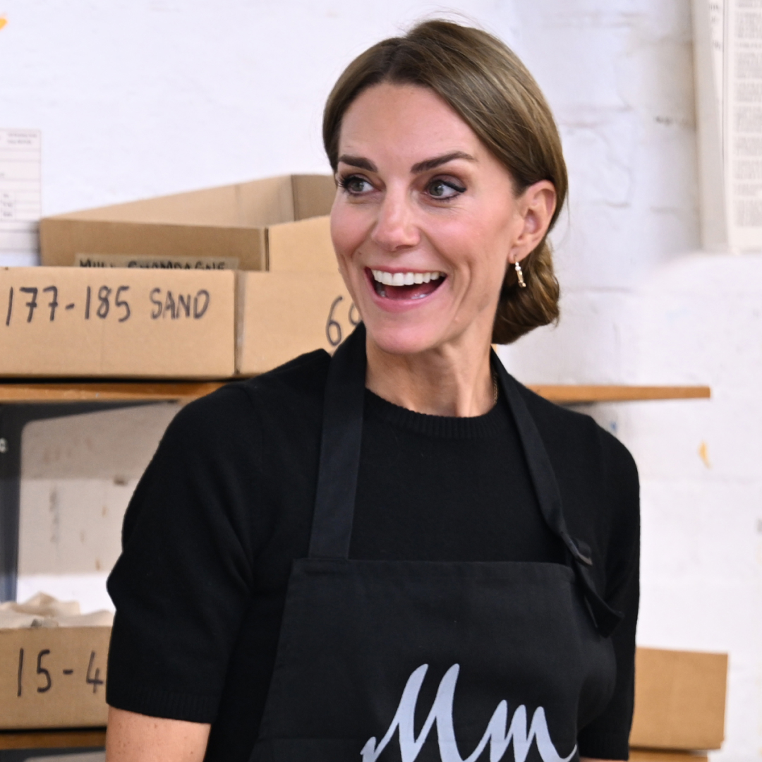 Kate Middleton wearing a black shirt and apron with her hair in a knot 
