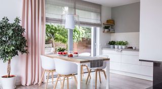 White kitchen with white table and chairs and pale pink curtains
