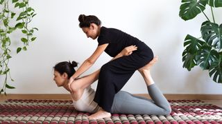 Woman on her stomach with partner standing over her and pulling her chest back