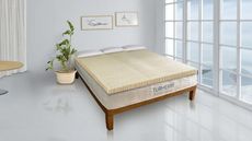 The Turmerry Latex Mattress Topper on a bed against a gray wall.