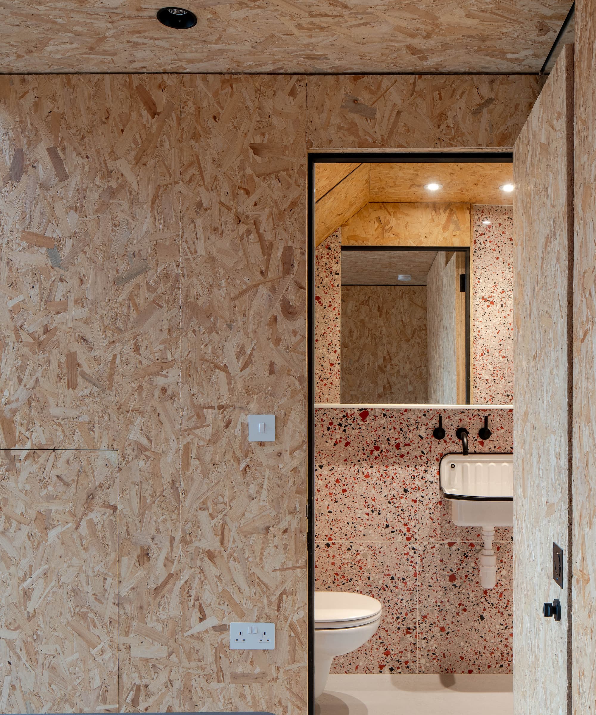 An en suite bathroom next to a plasterboard wall with a white toilet and sink and large mirror