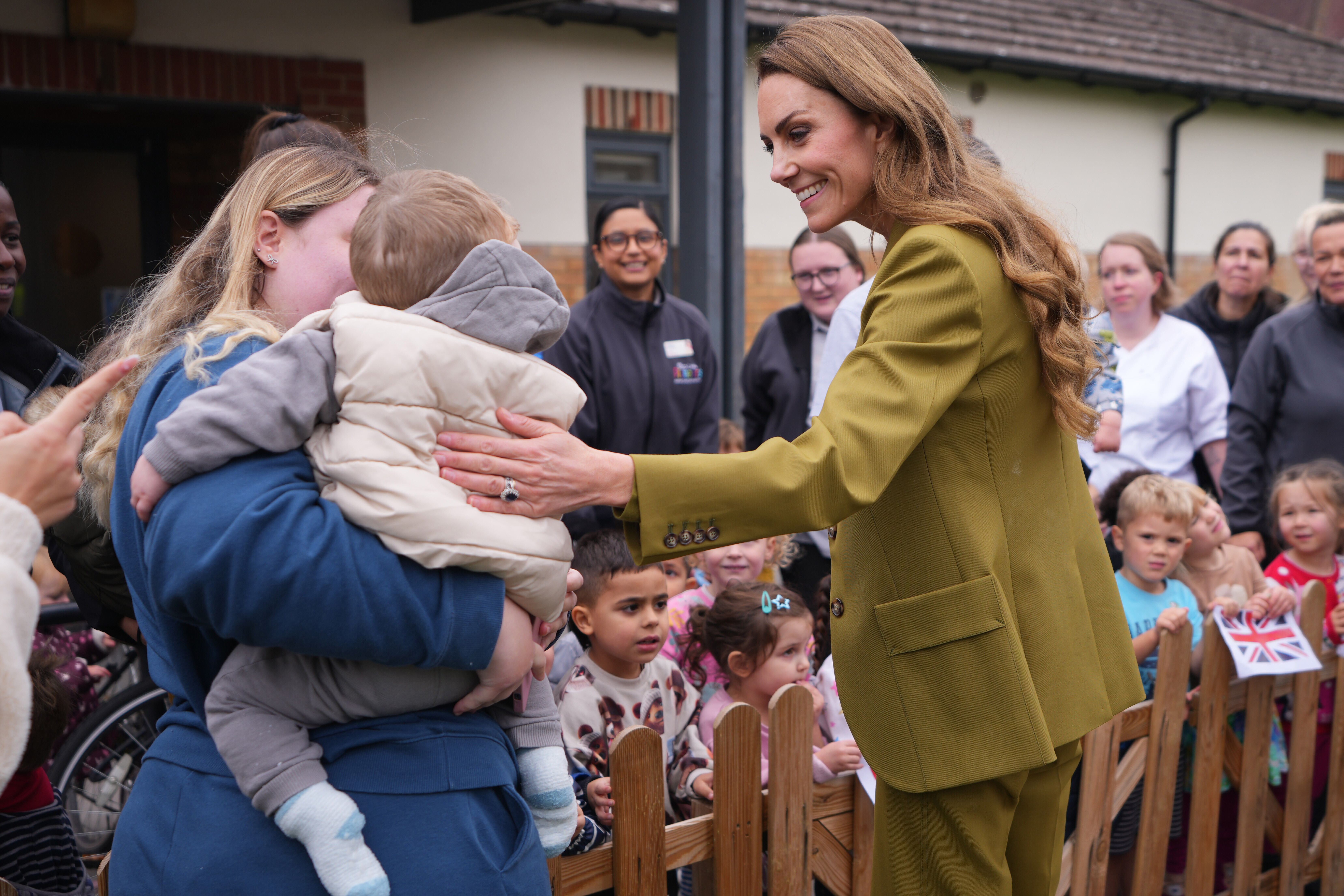 Kate Middleton wearing an olive green suit patting a baby on its back