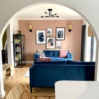 Living room with pink accent wall and navy sofas as seen through white painted archway