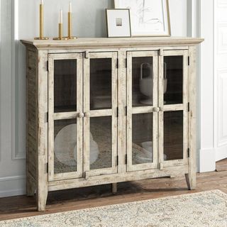 A light wooden distressed accent cabinet with glass paneled doors that's a part of Kelly Clarkson's furniture collection.