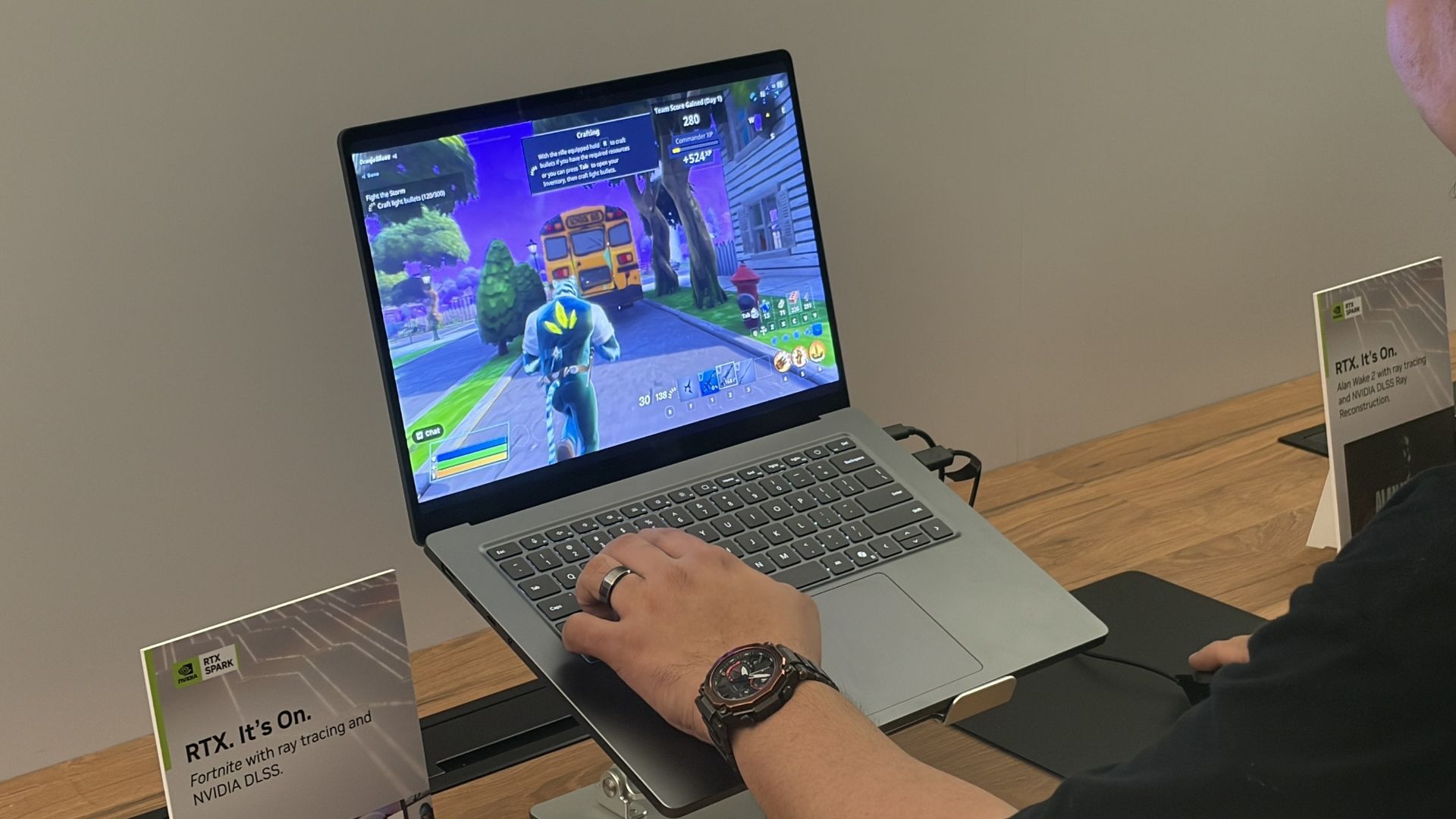 A person plays Fortnite on a Surface Laptop UItra at a display table, with NVIDIA RTX signs nearby; the colorful game scene feels lively and immersive.