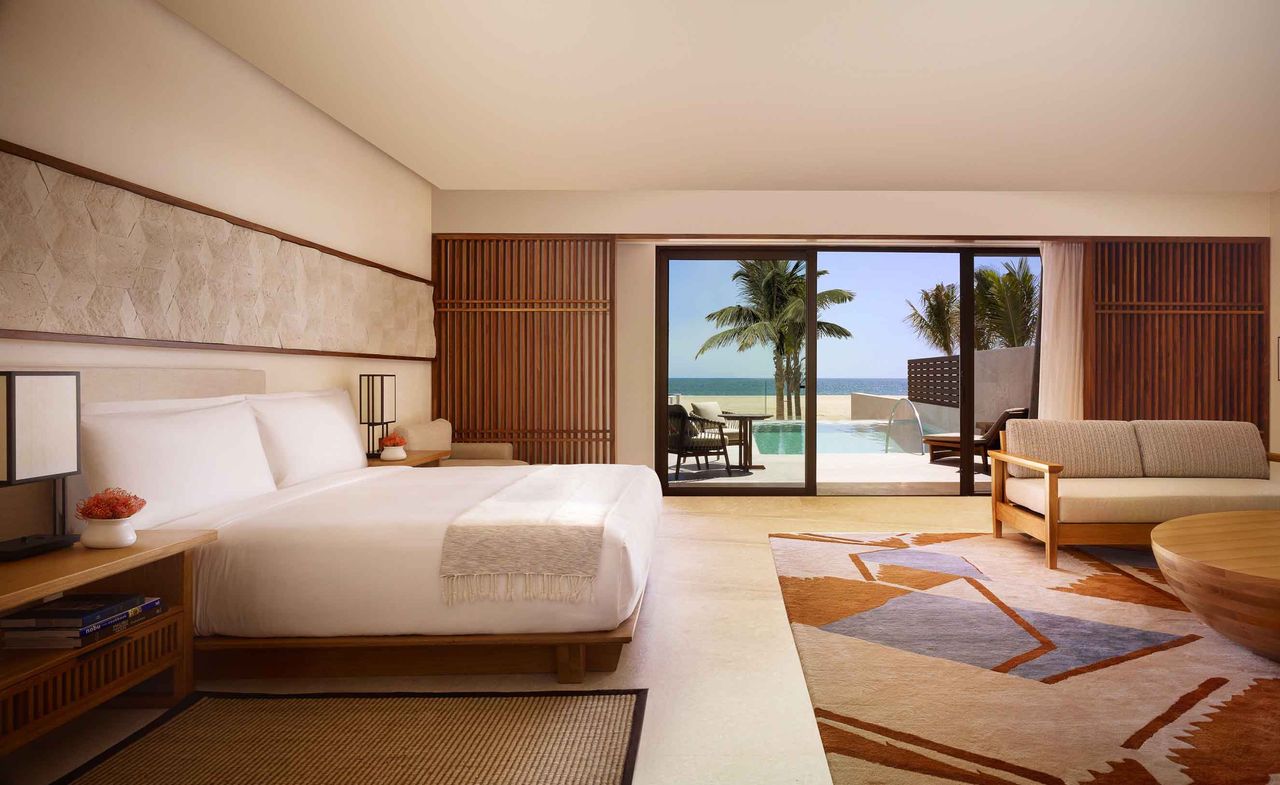 Nobu Hotel spacious bedroom with cream walls, cream sofa, round wooden table and white linen